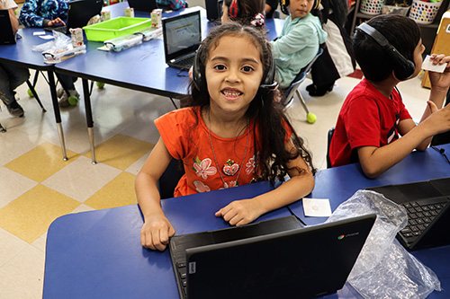 A girl wearing headphones smiling with a laptop in front of her